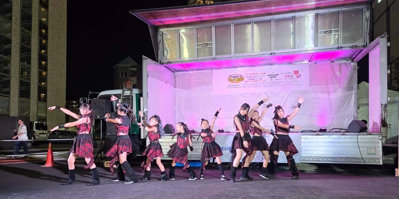 赤いチェックの衣装をそろえて駅前広場のステージで踊る生徒たち